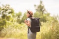 Stylish hipster girl in straw hat traveling countryside. Young woman with backpack exploring and walking in summer nature park. Royalty Free Stock Photo