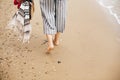 Stylish hipster girl walking barefoot on beach, holding bag and shoes in hand, closeup. Summer vacation. Space for text. Calm Royalty Free Stock Photo