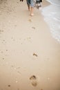 Stylish hipster girl walking barefoot on beach, holding bag and shoes in hand. Footprints on sand close up. Summer vacation. Space Royalty Free Stock Photo