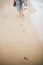 Stylish hipster girl walking barefoot on beach, holding bag and shoes in hand. Footprints on sand close up. Summer vacation. Space Royalty Free Stock Photo