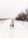 Stylish hipster girl walking with cute golden dog in snowy cold park. Woman taking walk with her dog in winter white forest. Phone