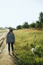 Stylish hipster girl walking with cute white puppy in summer park. Young woman on a walk with her doggy in warm sunshine light. Royalty Free Stock Photo