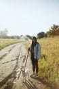 Stylish hipster girl walking with cute white puppy in summer park. Young woman on a walk with her doggy in warm sunshine light. Royalty Free Stock Photo