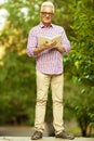 Stylish hipster grandpa concept. Portrait of smiling trendy handsome mature man with eyeglasses walking in the park and reading Royalty Free Stock Photo