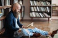 Stylish hipster man reading book sitting on floor in library Royalty Free Stock Photo