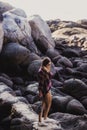 Stylish hipster woman in checkered shirt and shirts on summer beach at sunset. Path in a rocks at beach