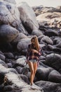 Stylish hipster woman in checkered shirt and shirts on summer beach at sunset. Path in a rocks at beach