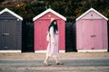 Stylish hipster woman with color hair in pink outfit and backpack walking along wooden beach huts on seaside. Off season