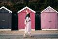 Stylish hipster woman with color hair in pink outfit and backpack walking along wooden beach huts on seaside. Off season