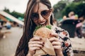 stylish hipster woman eating juicy burger. boho girl biting cheeseburger, smiling at street food festival. summertime. summer vac