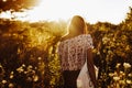 stylish hipster woman with eco bag walking in sunlight among wildflowers in summer evening field under sun rays. atmospheric Royalty Free Stock Photo