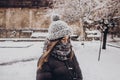 stylish hipster woman in knitted hat standing in snowy city street. beautiful fashionable girl in warm clothes in cold snow Royalty Free Stock Photo