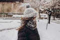 stylish hipster woman in knitted hat standing in snowy city street. beautiful fashionable girl in warm clothes in cold snow Royalty Free Stock Photo