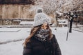 stylish hipster woman in knitted hat standing in snowy city street. beautiful fashionable girl in warm clothes in cold weather wi Royalty Free Stock Photo