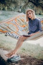 Stylish hipster woman reading book and relaxing in hammock in sunny summer park. blonde girl resting in forest, smiling and