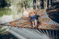 Stylish hipster woman relaxing in hammock in sunny summer park. blonde girl in fashionable hat resting in forest, smiling and Royalty Free Stock Photo