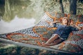 Stylish hipster woman relaxing in hammock in sunny summer park. blonde girl in fashionable hat resting in forest, smiling and Royalty Free Stock Photo