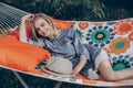 Stylish hipster woman relaxing in hammock in sunny summer park. blonde girl in fashionable hat resting in forest, smiling and