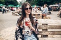 stylish hipster woman in sunglasses with lemonade, smiling. boho girl in denim and bohemian clothes, holding cocktail sitting on