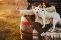 Stylish hipster woman taking selfie photo with cute dog in car trunk in warm sunset light. Autumn road trip with pet. Young female Royalty Free Stock Photo