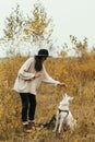 Stylish hipster woman training cute white dog on background of autumn trees. Traveling with pet