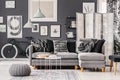 Industrial coffee table with vase and plate next to grey scandinavian corner sofa with pillows in monochromatic interior