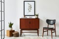 Stylish interior design of living room with wooden retro commode, chair, plant, rattan decoration, cube.