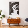 Stylish interior design of living room with wooden retro commode, white armchair, footrest and elegant personal accessories.