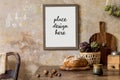 Stylish interior of kitchen space with wooden table, brown mock up photo frame, herbs, vegetables, tea pot, cups and kitchen. Royalty Free Stock Photo