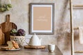 Stylish interior of kitchen space with wooden table, brown mock up photo frame, herbs, vegetables, tea pot, cups and kitchen. Royalty Free Stock Photo