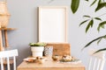 Stylish interior of kitchen space with wooden table with mock up photo frame, design chairs, decoration and furniture.