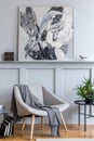 Stylish interior of living room with design grey armchair, pillows, coffee table, paintings, plant, decoration.