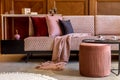 Stylish interior of living room with design pink velvet sofa, elegant pouf, coffee table, plant, pillows, decorations.