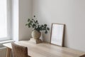 Stylish interior. Living room with poster frame mock up on wooden table, desk. Eucalyptus tree branches, rattan chair Royalty Free Stock Photo