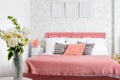 Stylish interior of modern bedroom. White and pink design of cozy bedroom with flowers. King-size bed with pink and grey bedding Royalty Free Stock Photo