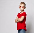 Stylish kid boy child in red t-shirt, jeans and sunglasses standing with hands crossed looking at camera Royalty Free Stock Photo