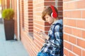 Stylish kid boy with headphones using phone at city street. Young boy plays online game at smartphone. Preteen boy listens to the