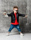 Stylish kid boy millionaire in sunglasses and leather jacket is cool posing with bundles of cash in both hands