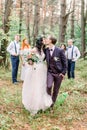 Stylish kissing bride and groom stand in front of the couples of bridesmaids and groomsmen in the forest. Wedding in