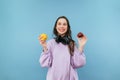 Stylish lady in headphones around her neck and purple sweatshirt posing at camera with apples in her hands on a purple background