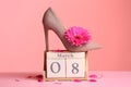 Stylish lady`s shoe, flower and wooden block calendar on table against color background.
