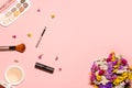 Stylish layout on a pastel pink background with makeup products: lipstick, beige powder, shiny eyeshadow palette, brushes; and