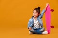 Stylish little child girl with skateboard in denim on orange background Royalty Free Stock Photo