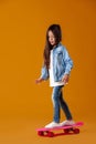 Stylish little child girl with skateboard in denim on orange background Royalty Free Stock Photo