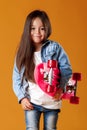 Stylish little child girl with skateboard in denim on orange background Royalty Free Stock Photo