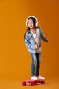 Stylish little child girl with skateboard in denim on orange background Royalty Free Stock Photo