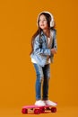 Stylish little child girl with skateboard in denim on orange background Royalty Free Stock Photo