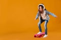 Stylish little child girl with skateboard in denim on orange background Royalty Free Stock Photo