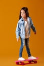 Stylish little child girl with skateboard in denim on orange background Royalty Free Stock Photo