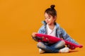 Stylish little child girl with skateboard in denim on orange background Royalty Free Stock Photo